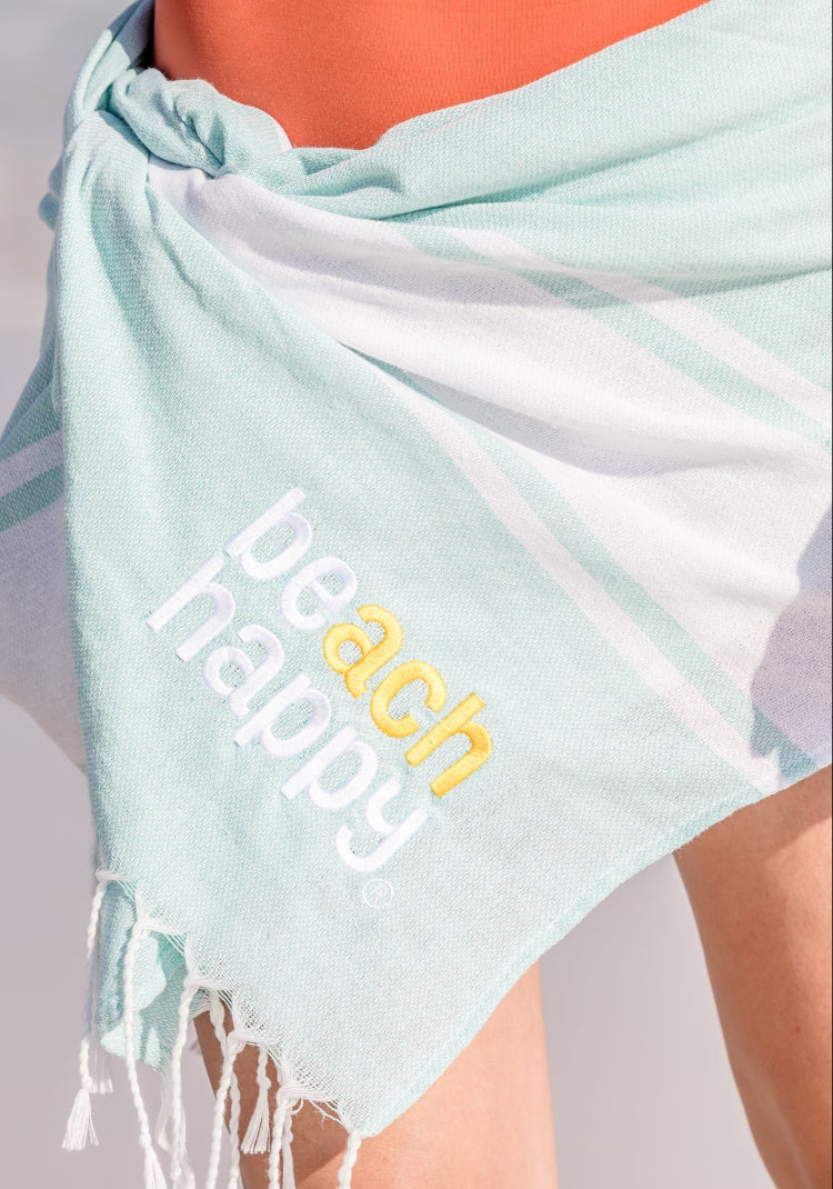 Light blue beach towel with 'beach happy' text on a blurred beach background